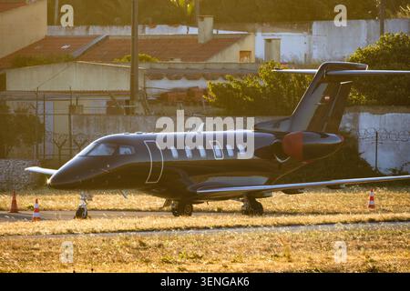 Private jet is parked on runway in residential area during sunset with buildings in the background and warm light Stock Photo