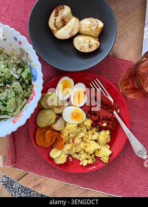 Millet porridge is served with baked vegetables and boiled eggs alongside beetroot hummus. Fresh salad adds crunch, and baked apples with spice comple Stock Photo