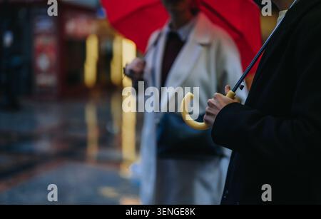 Two people holding umbrellas on a wet city street with a red umbrella in the foreground Stock Photo