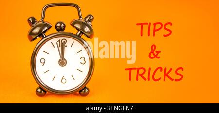 Tips and tricks words symbol. Concept words Tips and tricks on beautiful white paper. Beautiful orange background. Black alarm clock. Business tips an Stock Photo