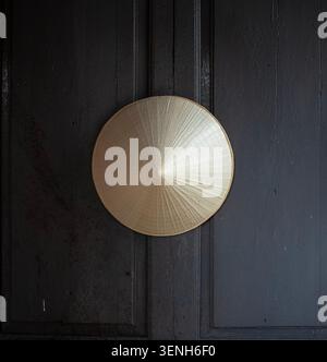 A traditional Vietnamese conical straw hat hanging symmetrically on a dark, rustic wooden door. Stock Photo