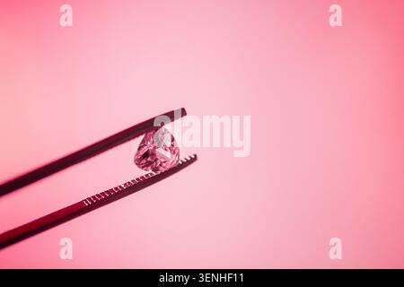 Close-up view of a diamond being held by tweezers against a soft pink backdrop, highlighting the gem's facets and clarity in a simple composition Stock Photo