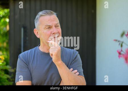 Thoughtful mature man standing outdoors with a reflective expression while considering future decisions. Natural lifestyle portrait representing plann Stock Photo
