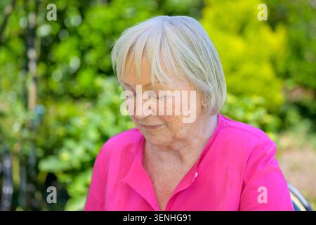 Close up portrait of a thoughtful senior woman sitting outdoors in a peaceful summer garden. Authentic lifestyle image representing aging, reflection, Stock Photo