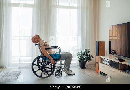 unhappy sad man in wheelchair sitting alone in living room leaning head back in frustration or exhaustion representing depression fatigue mental healt Stock Photo