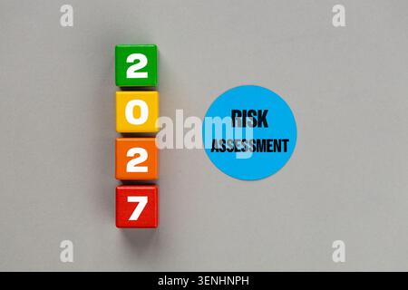 Risk assessment for year 2027 business concept with wooden toy blocks and blue paper circle on grey background. Flat lay, copy space Stock Photo