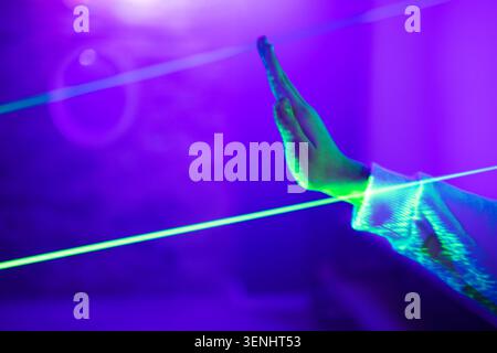 Hand positioned to touch green and blue laser beams in a dimly lit environment, with a purple hue creating a vibrant atmosphere Stock Photo
