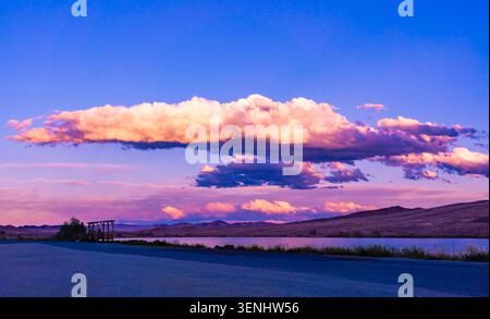 Blue Hour sun glow photography shows billowing clouds over mountains in Wyoming. Deep strong blue yellow shows shadows & glow on water in lake. Stock Photo