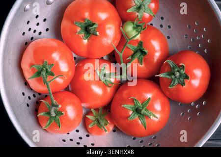 Colander full of ripe tomatoes on kitchen surface. Fresh washed vegetables, home cooking concept Stock Photo