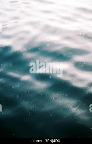 Raindrops Creating Ripples on Calm Water Surface Stock Photo