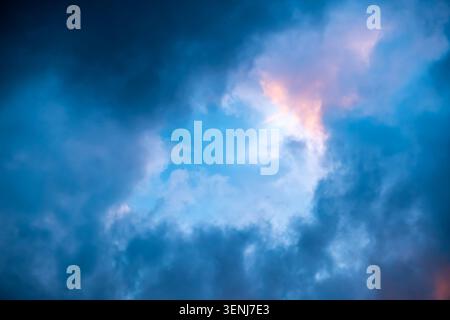 Dramatic sky full of dark clouds in bad weather before a big storm rain with a patch of light blue sky in center. Light emission from the Edge of Stock Photo