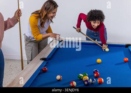Diverse friends playing pool, woman lining shot on pool table with cue, scattered balls, copy space Stock Photo