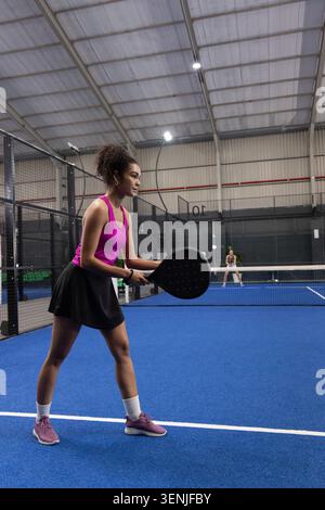 Diverse female players competing, African American in pink holding black padel racket on blue court Stock Photo