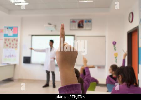 Close-up of a schoolgirl hand raised to ask a question in a classroom. Stock Photo