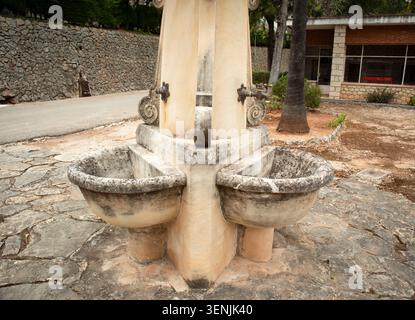 Close up view of an ancient stone drinking fountain with two basins in a rustic Mediterranean courtyard. The fountain shows wear and tear from years o Stock Photo