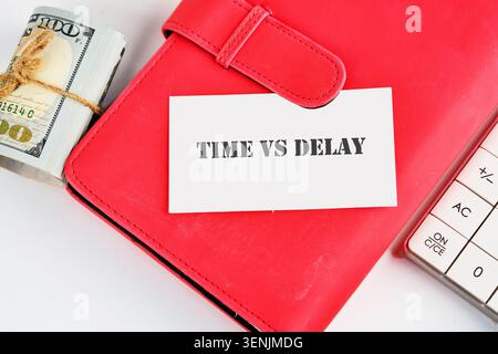 A red folder holds a card that says time vs delay. A stack of cash sits next to a calculator. This scene is set in an office during working hours Stock Photo