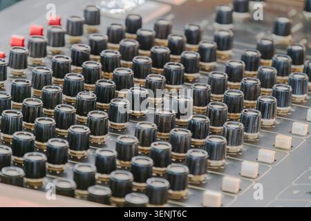 Professional audio mixing console close-up, featuring numerous black knobs with white centers, some with red caps for distinction, set against a dark Stock Photo
