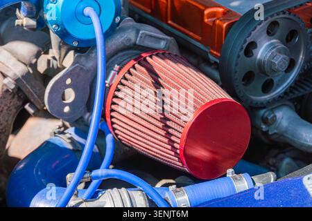 High-performance air intake system featuring cylindrical red filter with pleated media trapping contaminants, connected to flexible ribbed hose showca Stock Photo