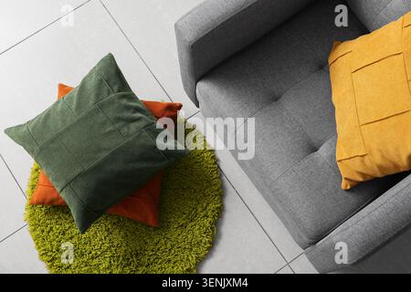 Modern living room interior design with gray sofa, green shaggy rug, and colorful decorative pillows on tiled floor Stock Photo