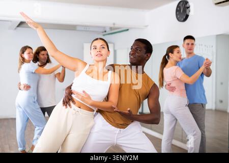 Joyful young adult couples learning passionate pair dancing during practicing in choreography class Stock Photo