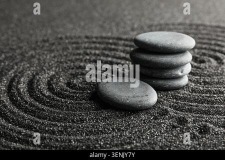 Stacked zen stones and single pebble on raked black sand, japanese garden meditation and balance Stock Photo