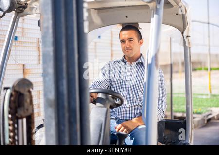 Attentive farmer man working on forklift loader at farm greenhouse Stock Photo