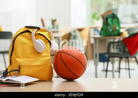 Yellow school backpack with headphones, basketball, and books on a classroom desk, back to school Stock Photo