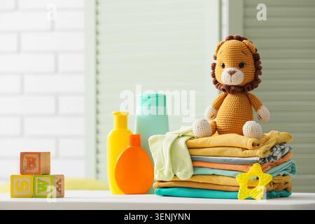 Baby care products and crocheted lion toy with stacked clothes and alphabet blocks on white surface, the scene includes various items for infant hygie Stock Photo