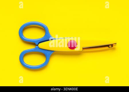 Colorful blue and yellow childrens safety scissors with red dot on bright yellow background Stock Photo