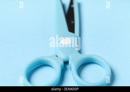 Light blue plastic handle scissors with metal blades on a soft blue background for crafting and office supplies, the tool is essential for various cut Stock Photo