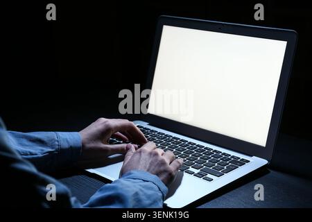 Person typing on laptop keyboard in dark room, cybersecurity and data privacy concept, online communication and digital work Stock Photo