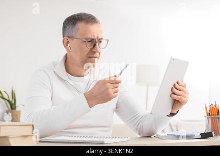 Focused mature man in glasses and earbuds using digital tablet with stylus for online learning or business, he is engaged in online learning or busine Stock Photo