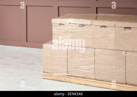 Stacked cardboard moving boxes wrapped in clear plastic on wooden pallet for shipping and storage Stock Photo
