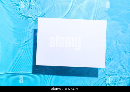 Blank white paper card floating on blue water surface with ripples and sunlight reflections, copy space for text or product display Stock Photo