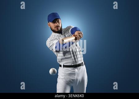 Professional baseball player hitting ball with bat, sports competition and athletic performance, blue background Stock Photo