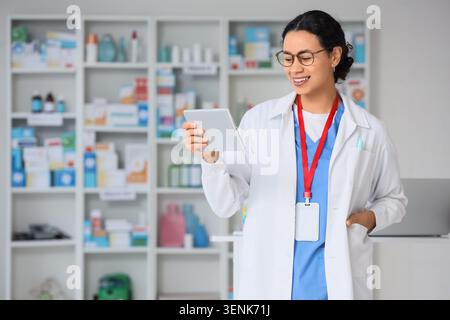 Smiling female pharmacist using digital tablet for inventory management in modern pharmacy with shelves of medicine Stock Photo