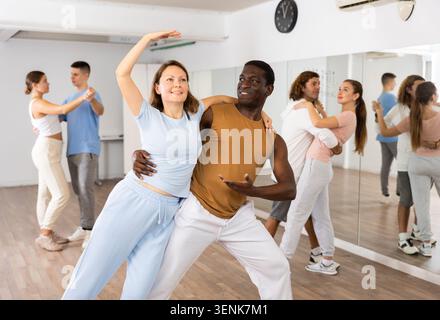 Smiling young adult couples dancing together in pairs and practicing new movements in modern studio Stock Photo