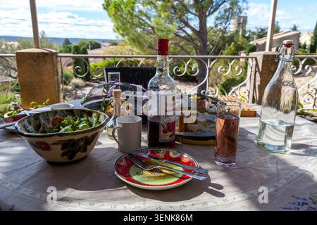 A rustic Provençal al fresco lunch table with colourful ceramic dishes, wine bottle, salad bowl and water on a sunny terrace in France Stock Photo