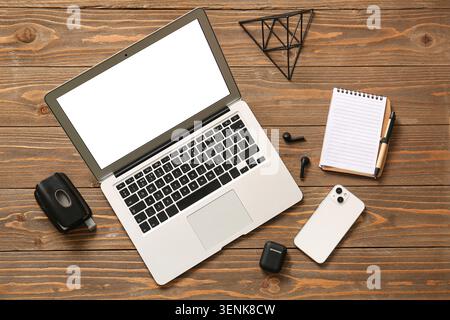 Modern laptop with blank screen, smartphone, earbuds, and notebook on rustic wooden desk for business and technology Stock Photo