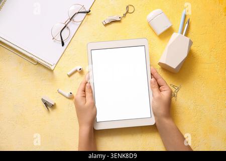 Hands holding digital tablet with blank screen on yellow desk with office supplies, top view, hands hold a digital tablet with a blank white screen Stock Photo