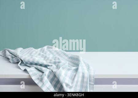 Light blue gingham fabric draped on white table with teal wall background for product display, the background features a solid teal wall, creating a m Stock Photo