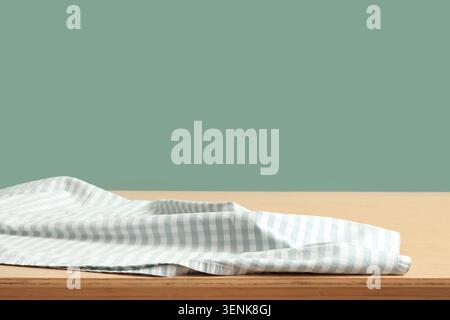 Empty wooden table with light blue gingham checkered fabric on green background for product display, the background is a solid green color, providing Stock Photo