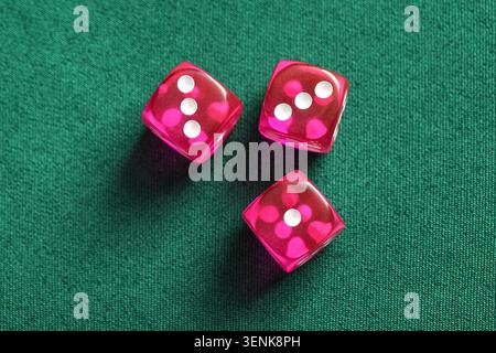 Three pink translucent dice with white dots on green felt table, gambling and chance game concept, the dice are arranged in a triangular pattern Stock Photo