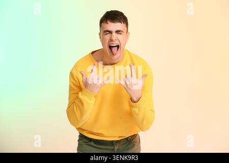 Young man in yellow sweatshirt making rock and roll hand gesture with tongue out and eyes closed, his eyes are closed and his tongue is sticking out, Stock Photo
