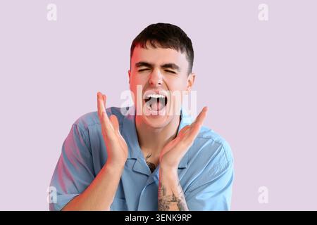 Young man shouting with hands raised, expressing extreme emotion, frustration, and stress on a light background Stock Photo