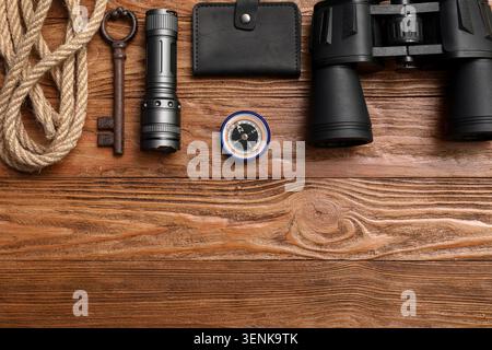Adventure exploration gear flat lay with binoculars, compass, flashlight, rope, and old key on rustic wooden background Stock Photo