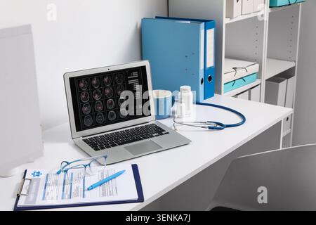 Medical office desk with laptop displaying brain scans, stethoscope, and health insurance form for healthcare technology Stock Photo