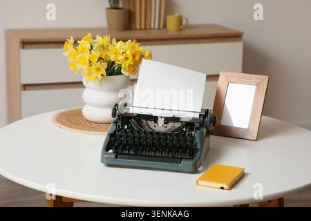 Vintage typewriter with blank paper, yellow daffodils, and wooden frame on white table for creative writing Stock Photo