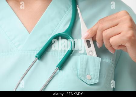 Medical professional with stethoscope and digital thermometer in pocket, healthcare and wellness, a hand places a white digital thermometer into the u Stock Photo