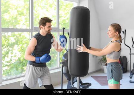 Man in boxing gloves training with punching bag, woman holding bag, fitness and healthy lifestyle Stock Photo